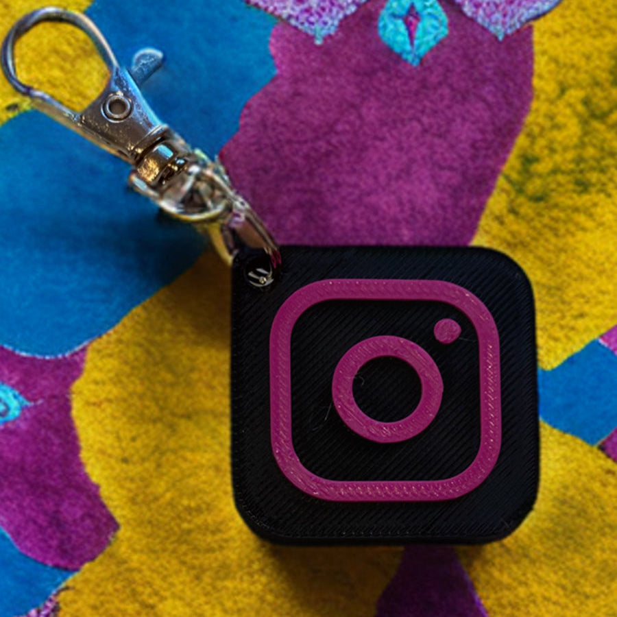 NFC tag  black and pink Instagram smart keyring with a 3D printed design, placed on a colorful textured background.